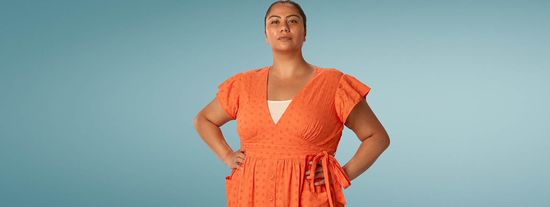Centered portrait of a confident looking woman in an orange dress.