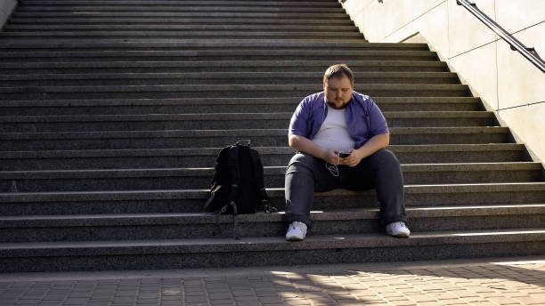Fat man listening to music on stairs, loneliness, overweight causes insecurities