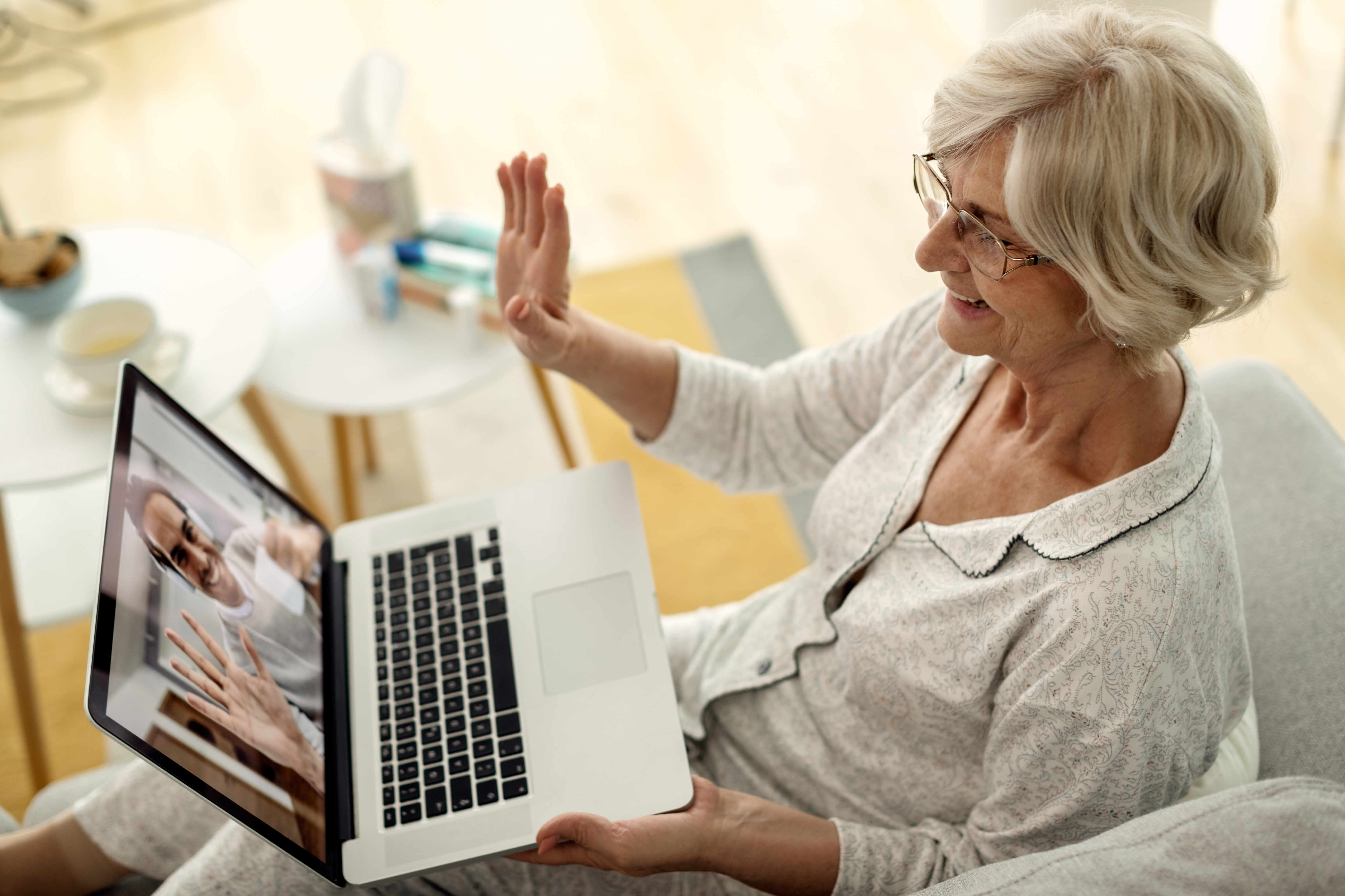 Happy mature woman using laptop and waving while talking to her son at home.